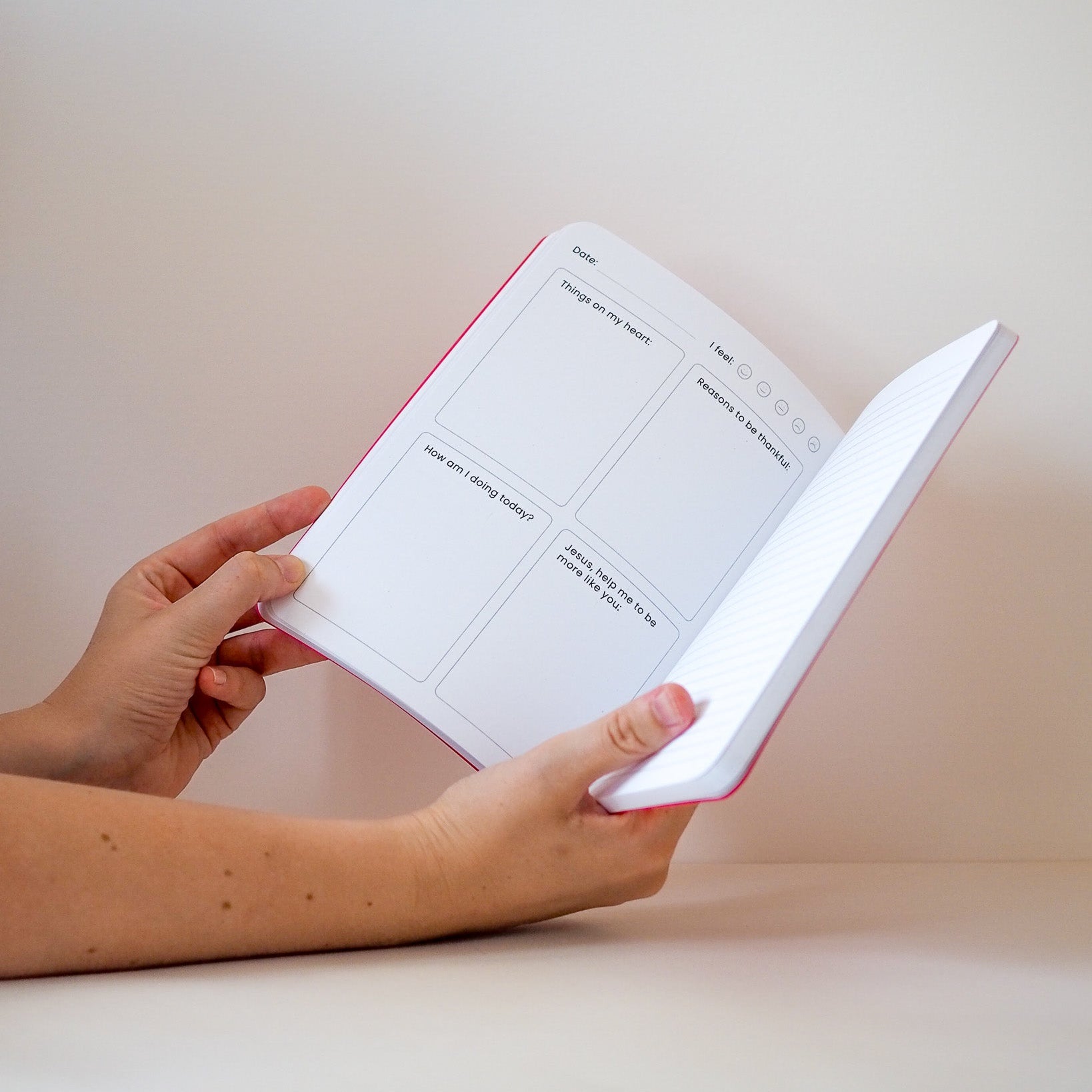Person holding a white prayer journal with pink edges against a plain background